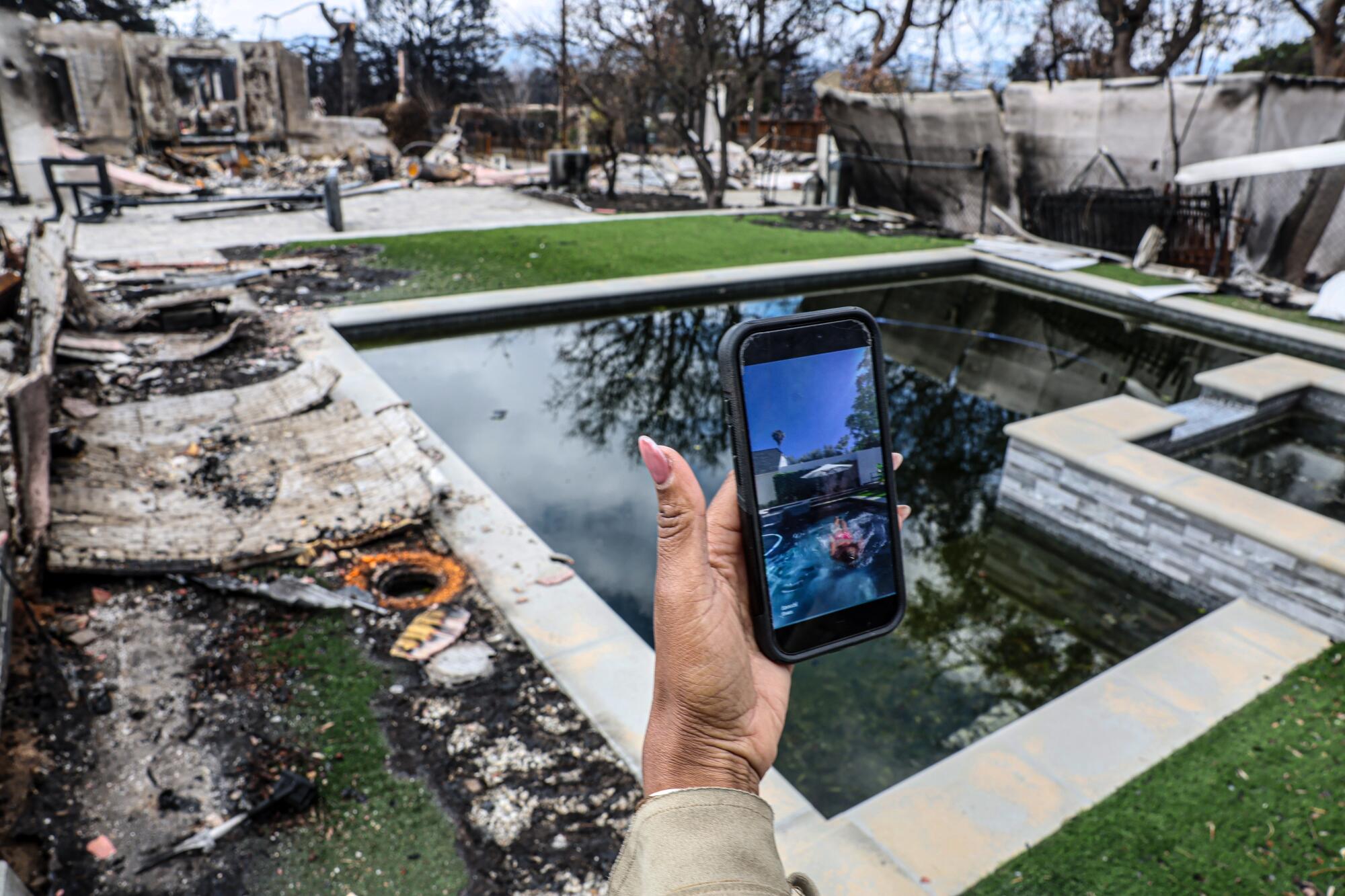 In a fire-damaged backyard with a dark pool, a woman shows a phone with a bright blue photo of the pool before.