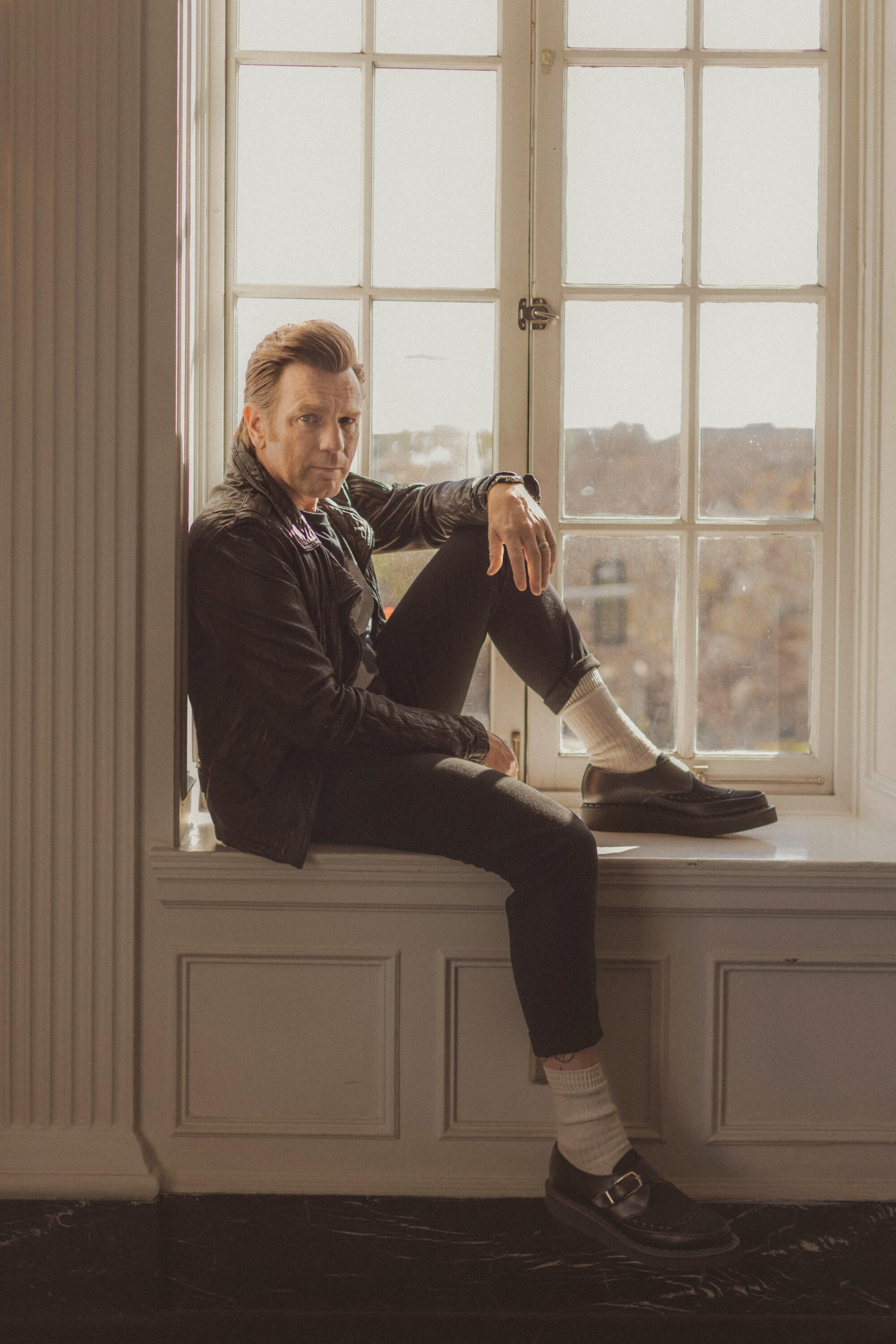 Ewan McGregor sits on a windowsill with one knee raised for a portrait.