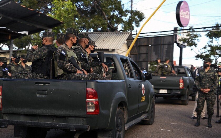 Soldiers ride in the back of pickup trucks at a street checkpoint in Tegucigalpa