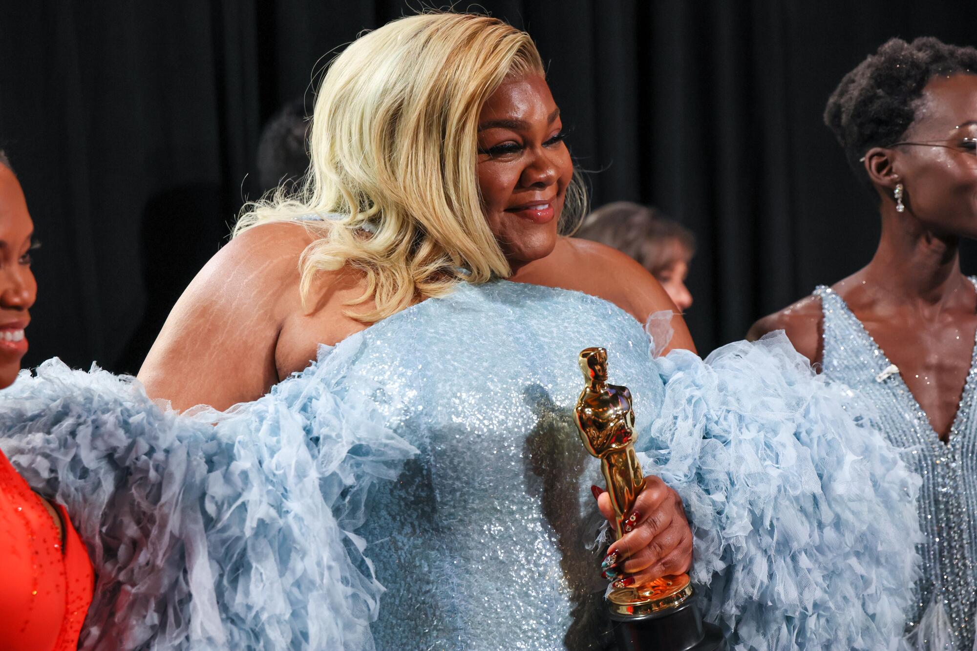 A blonde woman in a light blue dress holds an Oscar.