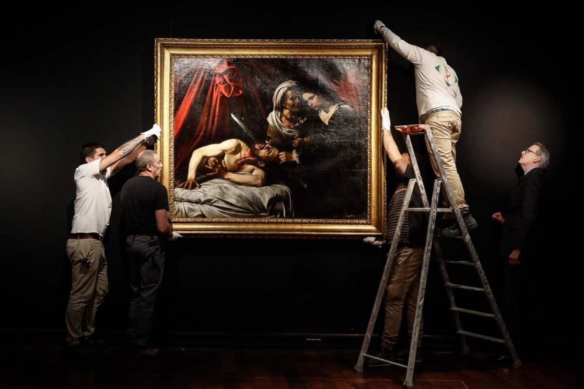 Workers hang the painting, attributed to Caravaggio, for its preview in Paris.