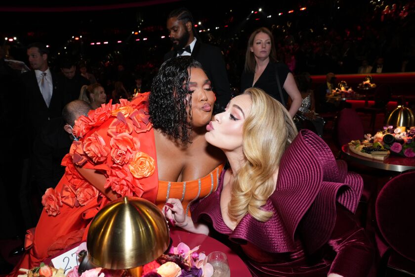 Lizzo in a bright orange grown and Adele in a purple gown almost kissing 