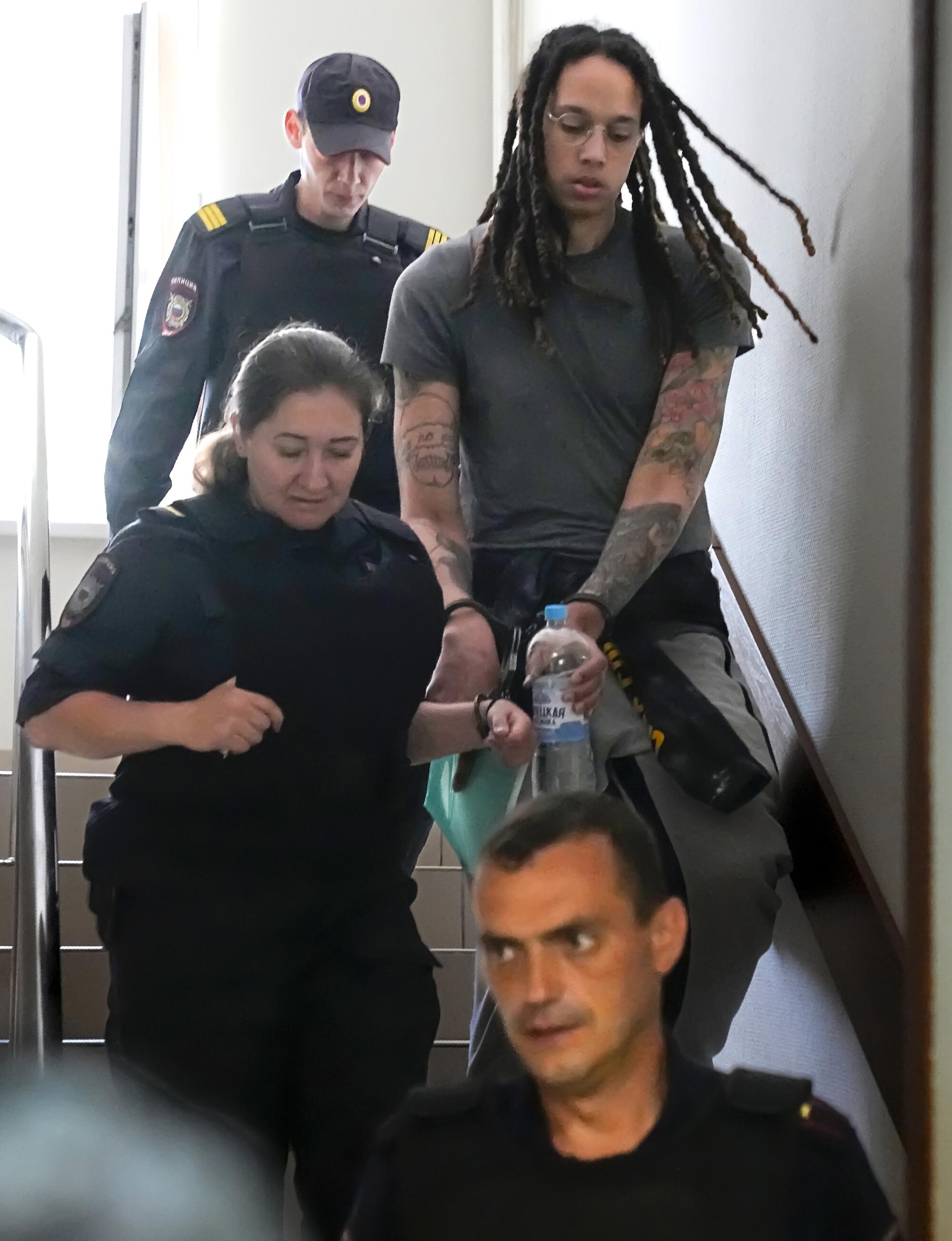 Brittney Griner in a stairwell, escorted by uniformed people.