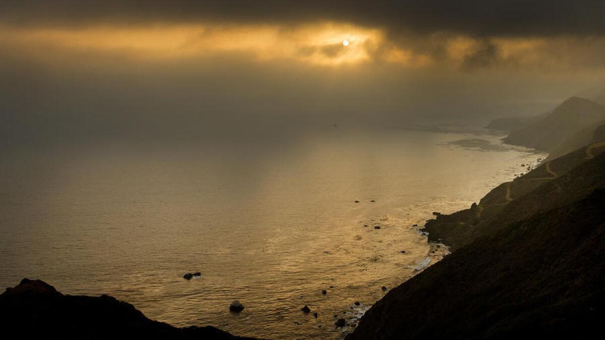 A scenic view of the setting sun shining through the fog along the Big Sur coastline.