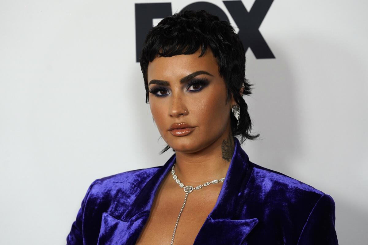 Demi Lovato poses for cameras in a purplish-blue suit jacket.
