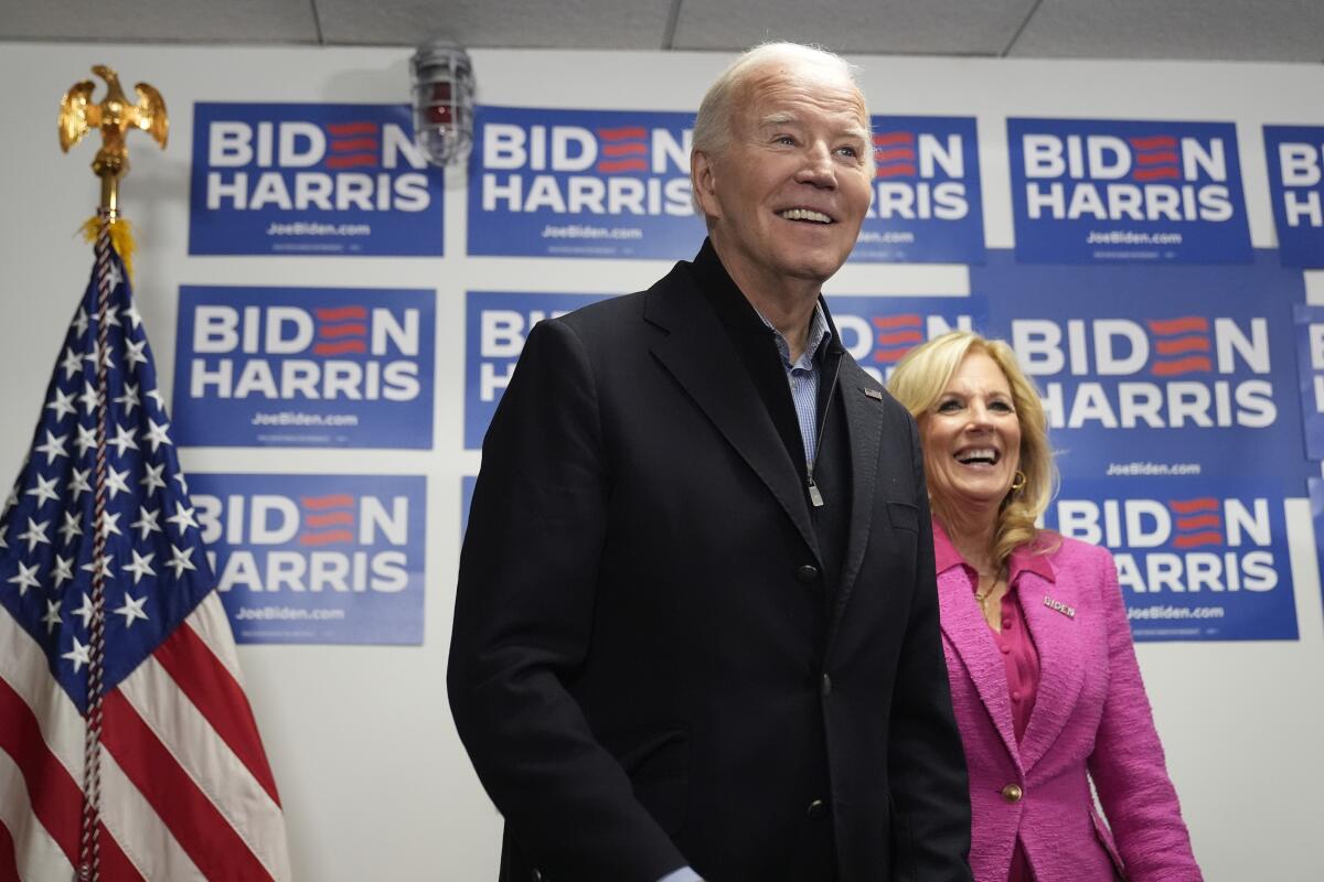 President Biden and wife Jill stand before a flag and campaign posters