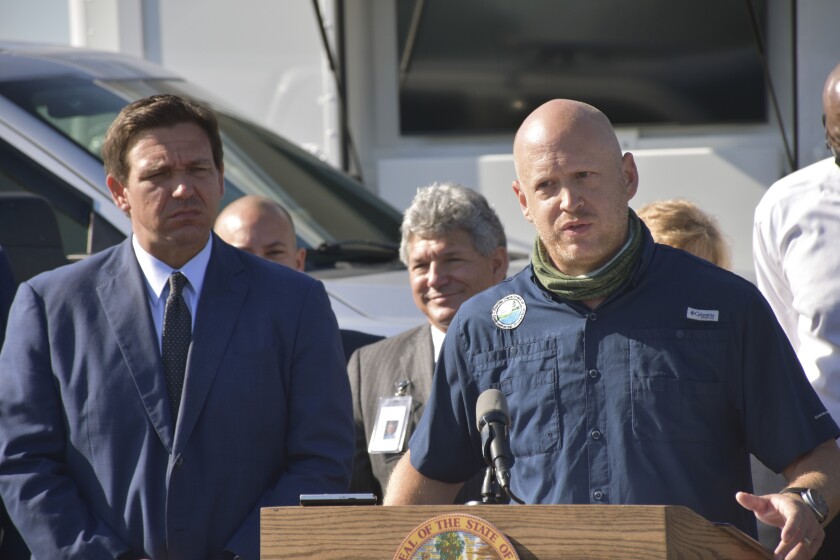 Florida Gov. Ron DeSantis, left, listens as Noah Valenstein, secretary of the Florida Department of Environmental Protection, right, speaks during a news conference at the Piney Point reservoir, Tuesday, April 13, 2021, in Palmetto, Fla. The governor said that Florida will permanently close the leaky Piney Point reservoir that poured millions of gallons of wastewater into Tampa Bay while threatening to burst open and flood nearby homes and businesses. (Ryan Callihan/The Bradenton Herald via AP)