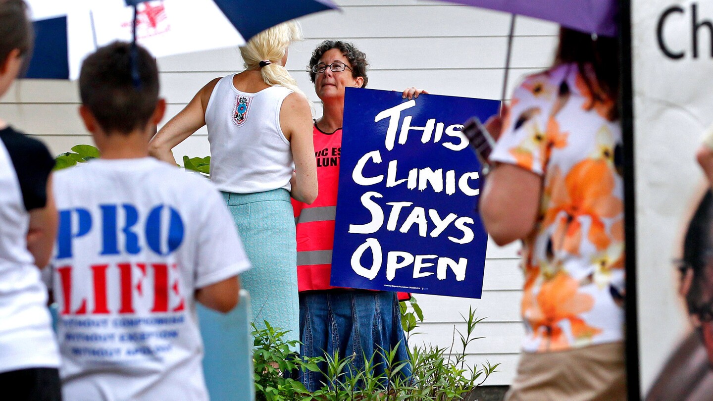 A volunteer at Causeway Medical Clinic in Metairie, La., stands at the entrance July 23 with a sign as antiabortion activists protest outside.