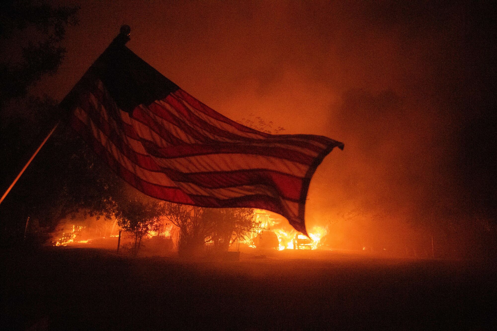 An American flag billows in front of a burning home in Vacaville, Calif.