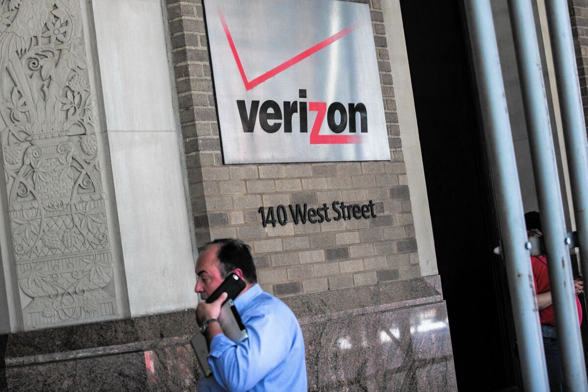 A man walks past a building adorned with a Verizon logo.
