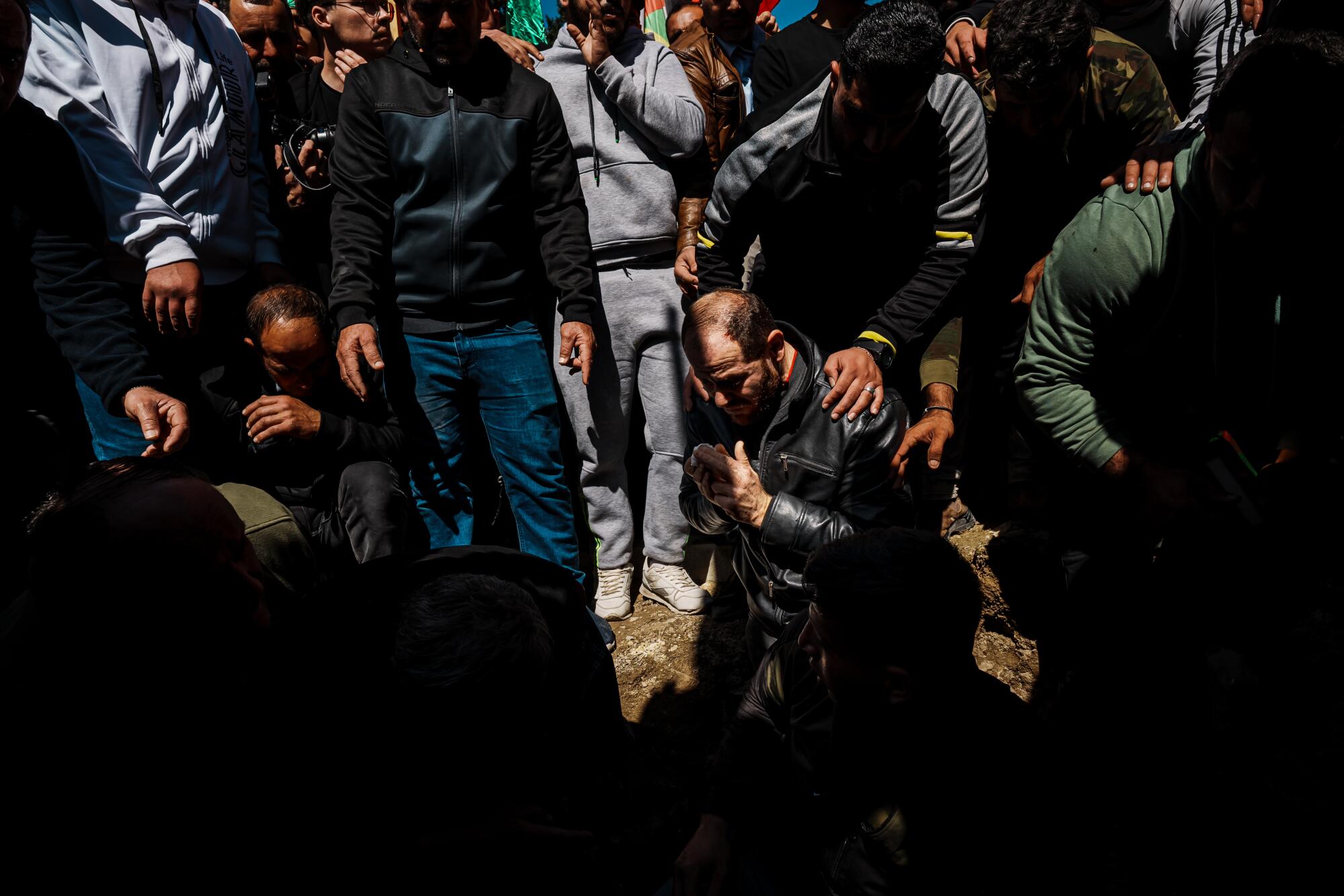 Mohammad Najjar kneels and is consoled after burying the body of his son Amro Najjar.