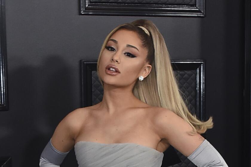 Ariana Grande in a gray tulle gown and matching gloves with a high ponytail posing with her hands on her hips