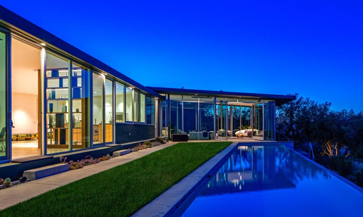 A house with glass walls overlooks an outdoor pool at night