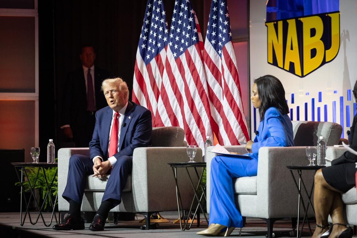 Former President Trump seated onstage with journalist Rachel Scott and a banner that reads, "NABJ" behind them