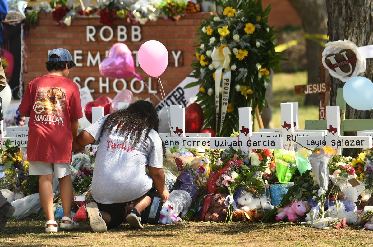 People kneel beside a memorial with crosses and flowers outside a school