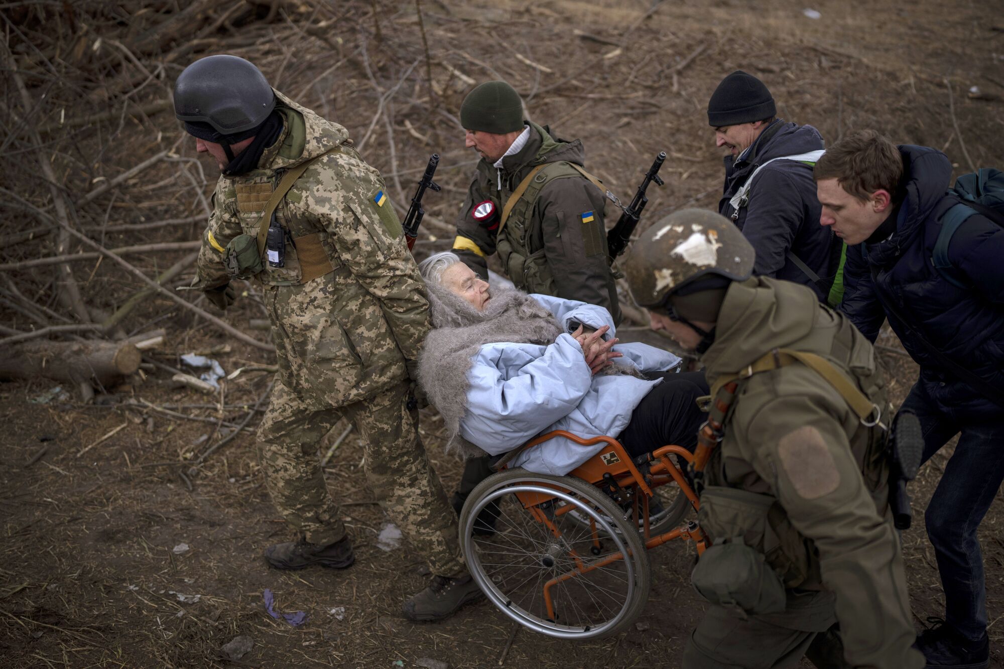 Ukrainian soldiers and militiamen carry a woman in a wheelchair while people flee Irpin on the outskirts of Kyiv, Ukraine.