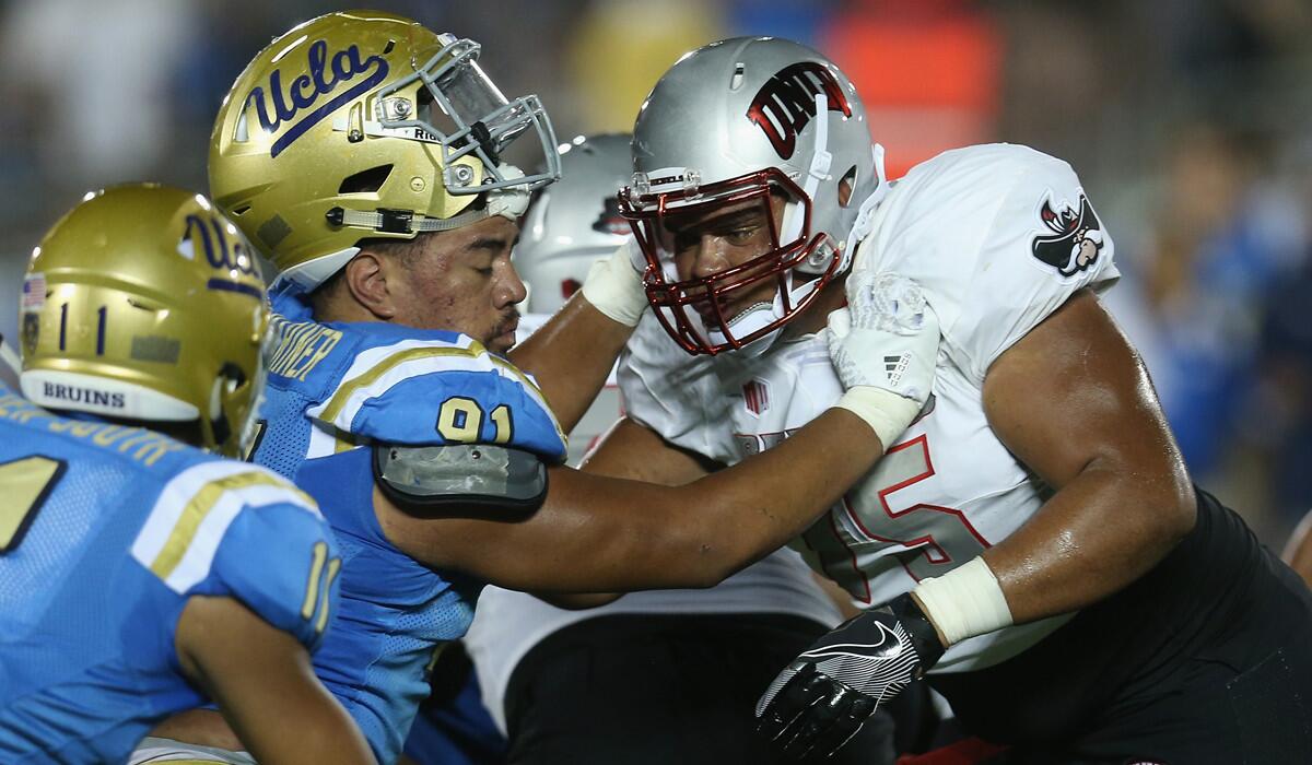 UCLA defensive end Jacob Tuioti-Mariner (91) partially loses his helmet as he battles UNLV offensive lineman Jaron Caldwell at the Rose Bowl on Saturday.