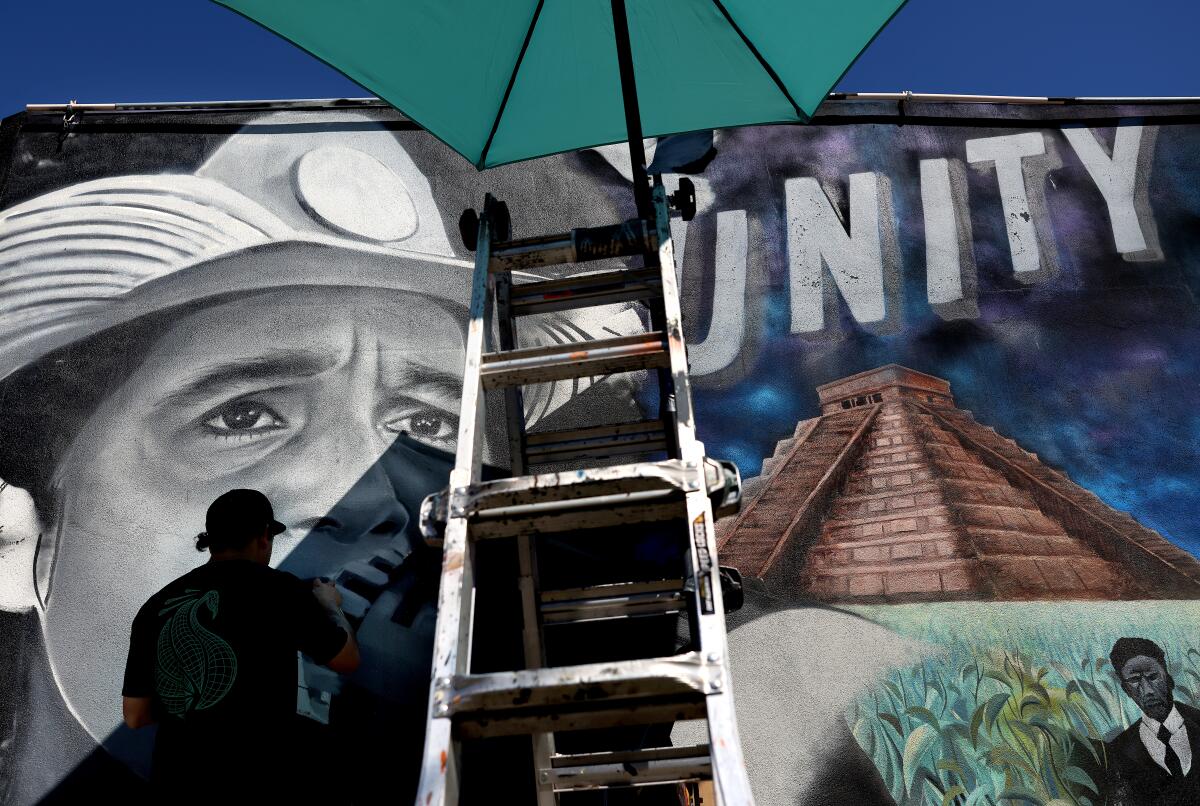 Artist MisterAlek replaces a portrait of César Chávez in a mural.