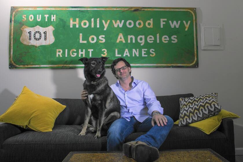 Ben Mankiewicz, second host on TCM, sits with his favorite dog, Bob, in front of an old stage prop sign at his home in Santa Monica.