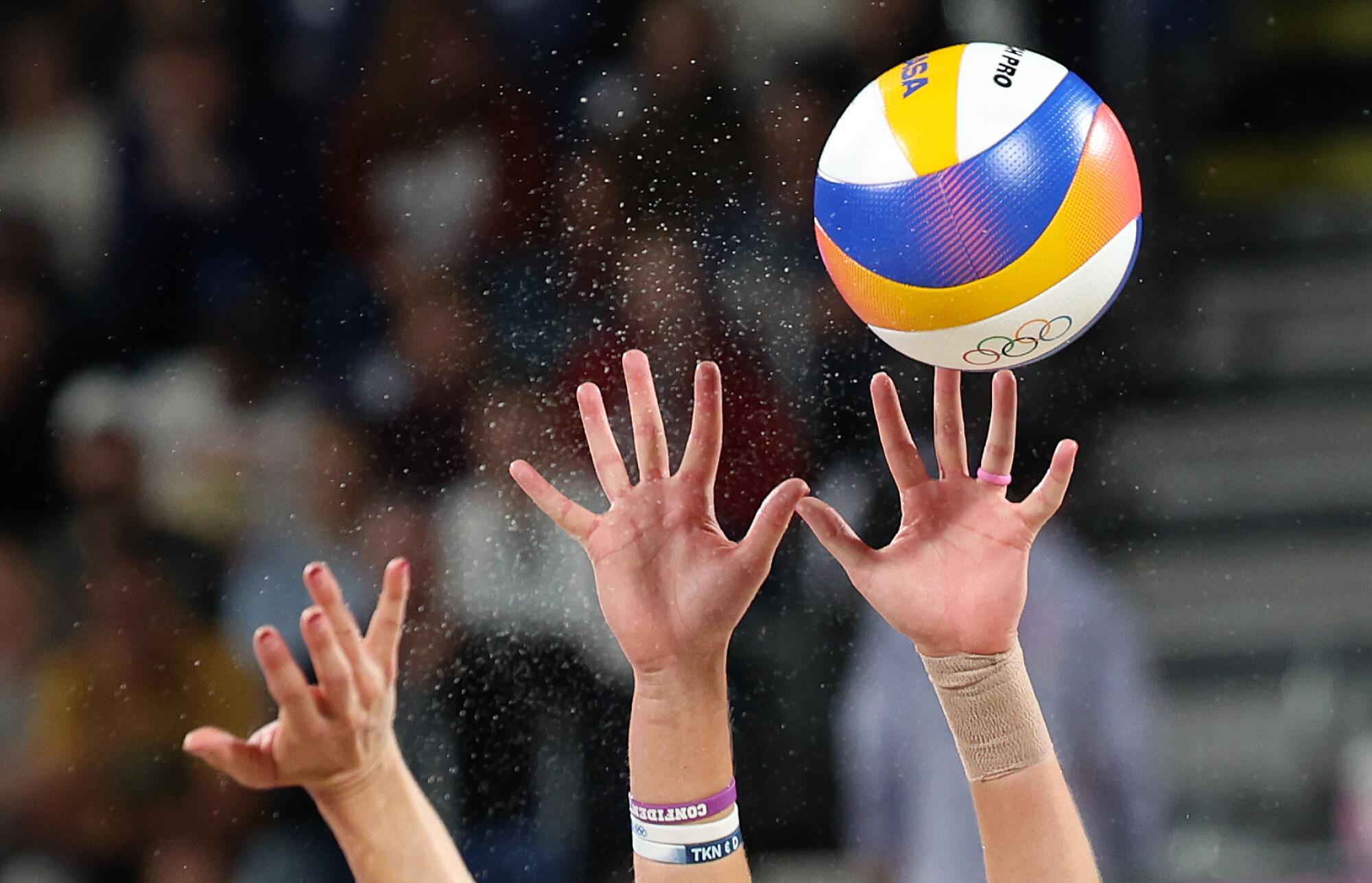 Hands reach for a volleyball.