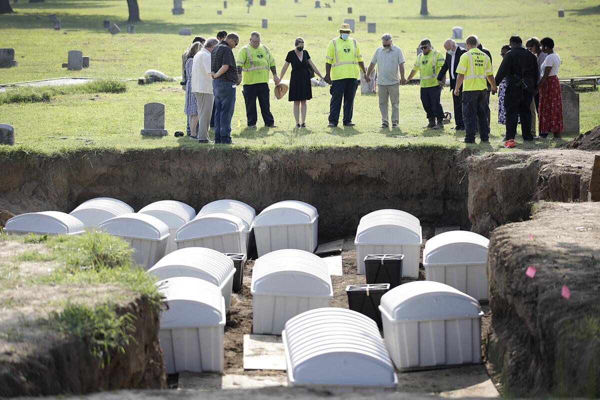 FILE - A group prays during a small ceremony as remains from a mass grave are re-interred at Oaklawn Cemetery, Friday, July 30, 2021, in Tulsa, Okla. The mass grave was discovered while searching for victims of the Tulsa Race Massacre. Scientists are planning to extract more DNA from the remains of possible Tulsa Race Massacre victims and to test two more areas as potential sites to search for more remains. The committee overseeing the project was told Tuesday, Sept. 13, 2022, that remains found last year and temporarily reburied in Oaklawn Cemetery will be exhumed for additional DNA samples in an effort to identify them, then reburied in the same location. (Mike Simons/Tulsa World via AP, File)