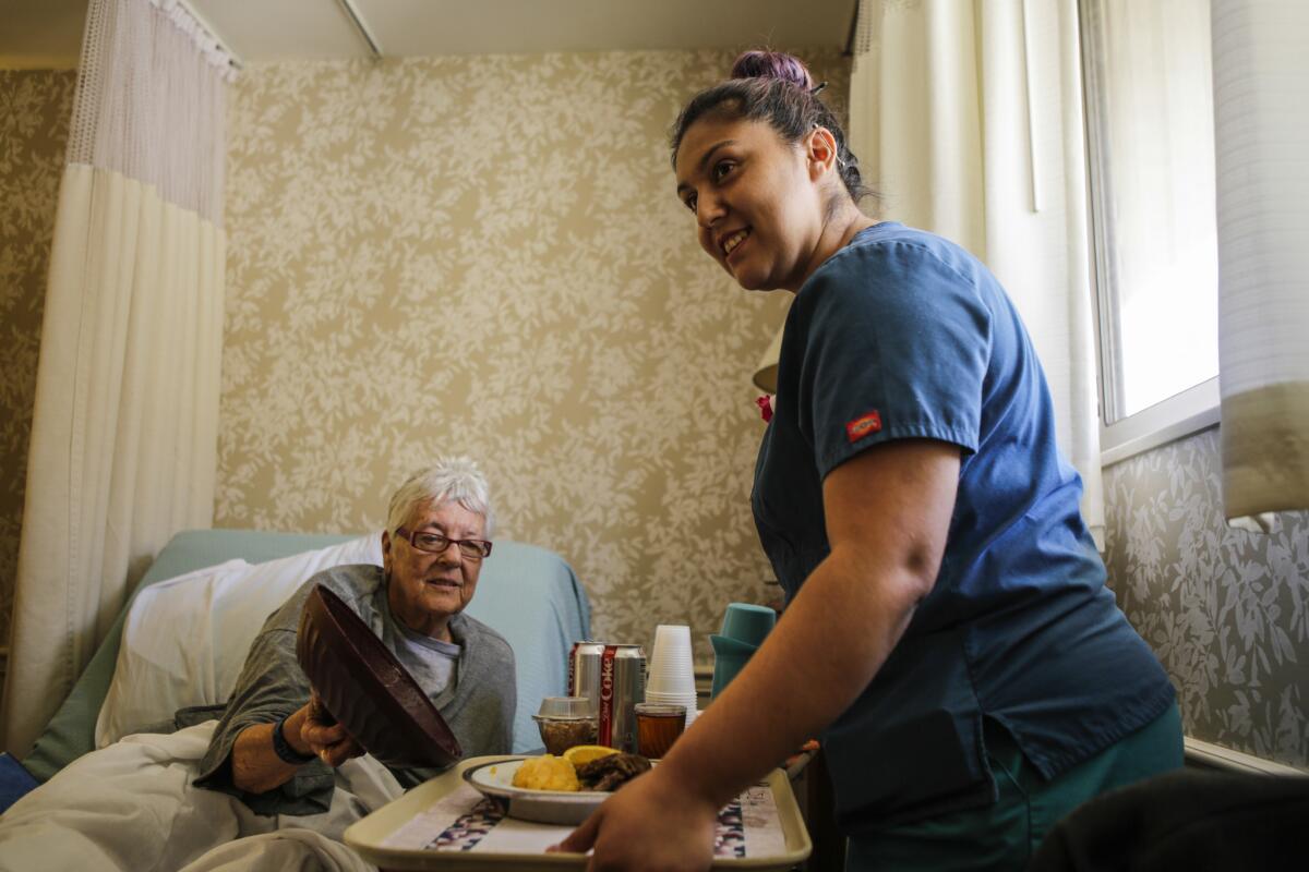 Gabby Carrillo, a certified nursing assistant, serves a patient a meal at the Californian-Pasadena, a nursing home in Pasadena. A new state law will require that patients receive a minimum number of hours per day from CNAs, but homes fear they won't meet the requirement.