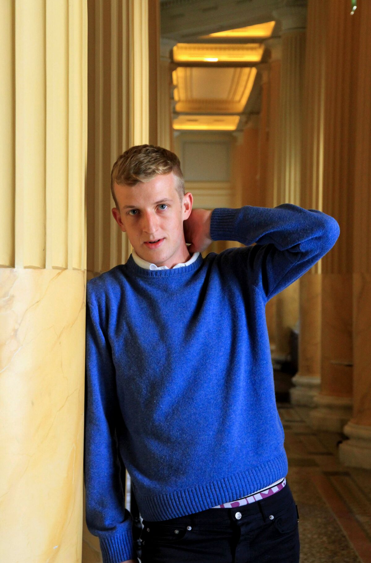 Man in blue sweater posses as he leans against a pillar