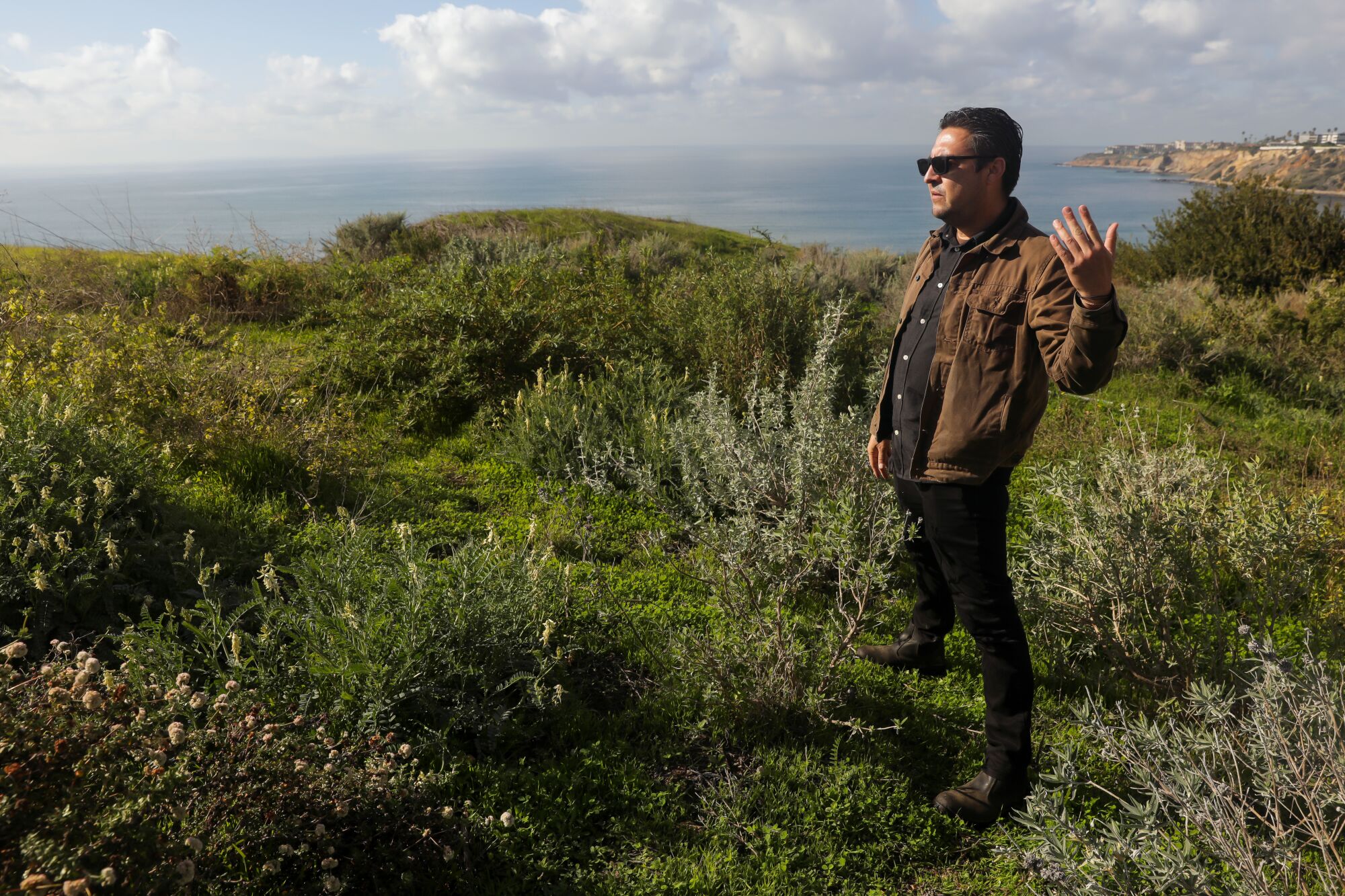 A man standing in a patch of green scrubland overlooking the ocean