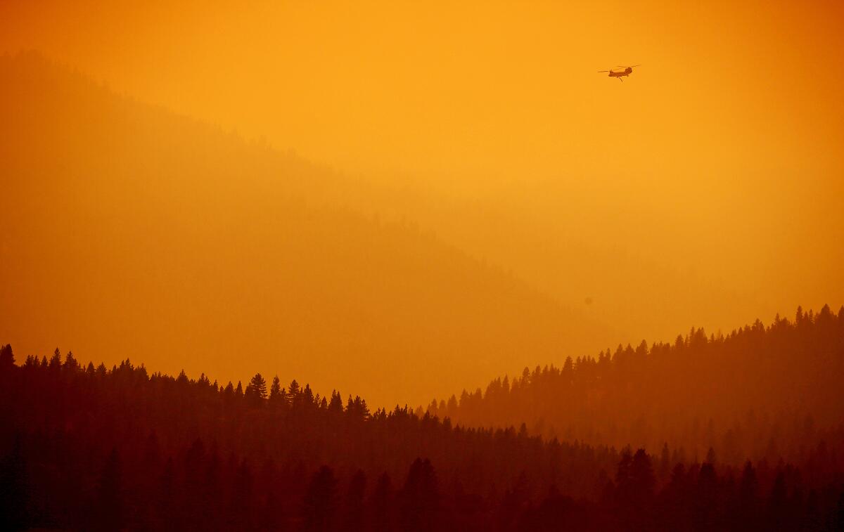 A helicopter flies over mountains blanketed in smoke from the Dixie fire near Janesville, Calif., in 2021.