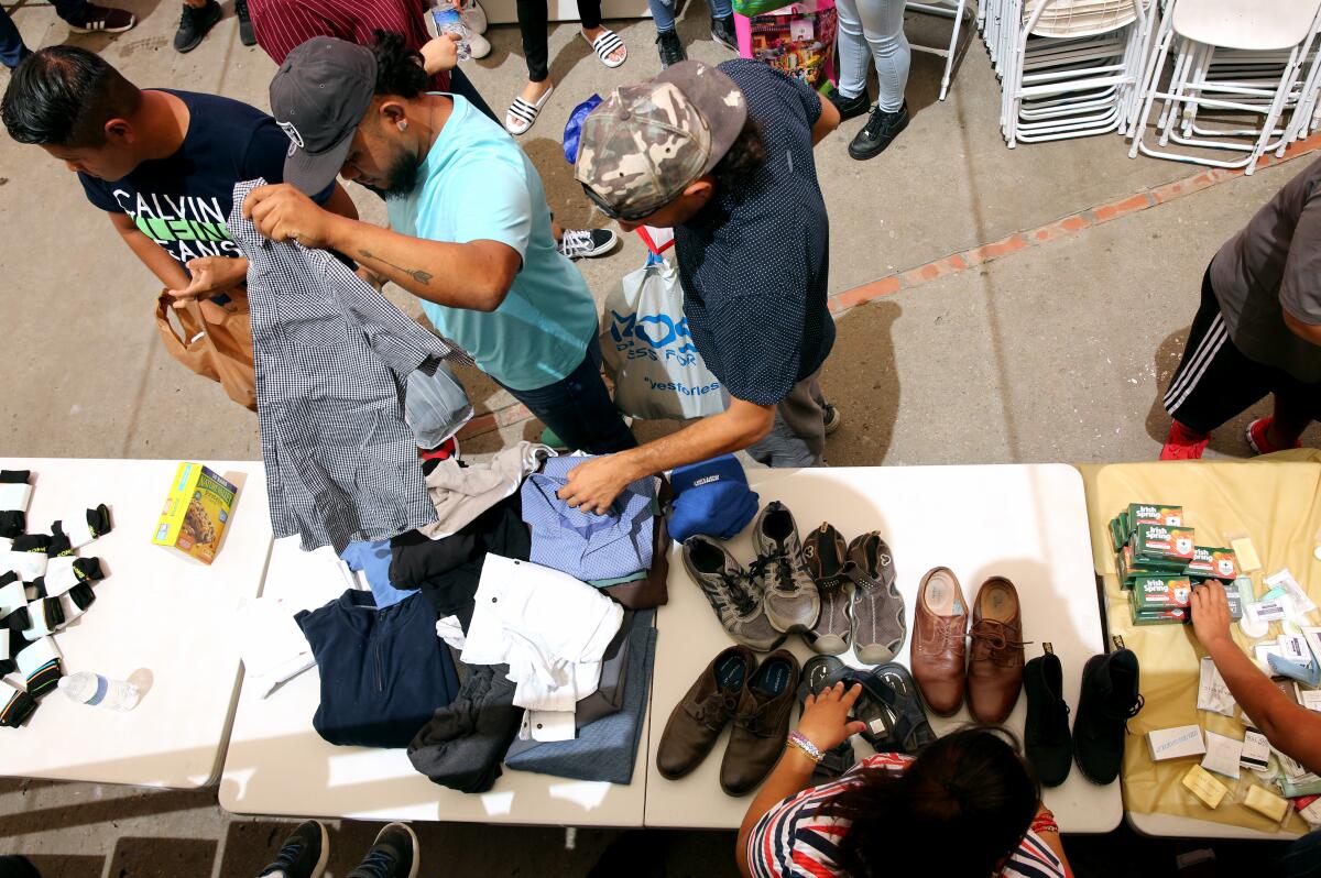 Men go through clothes, shoes and toiletries on a table.
