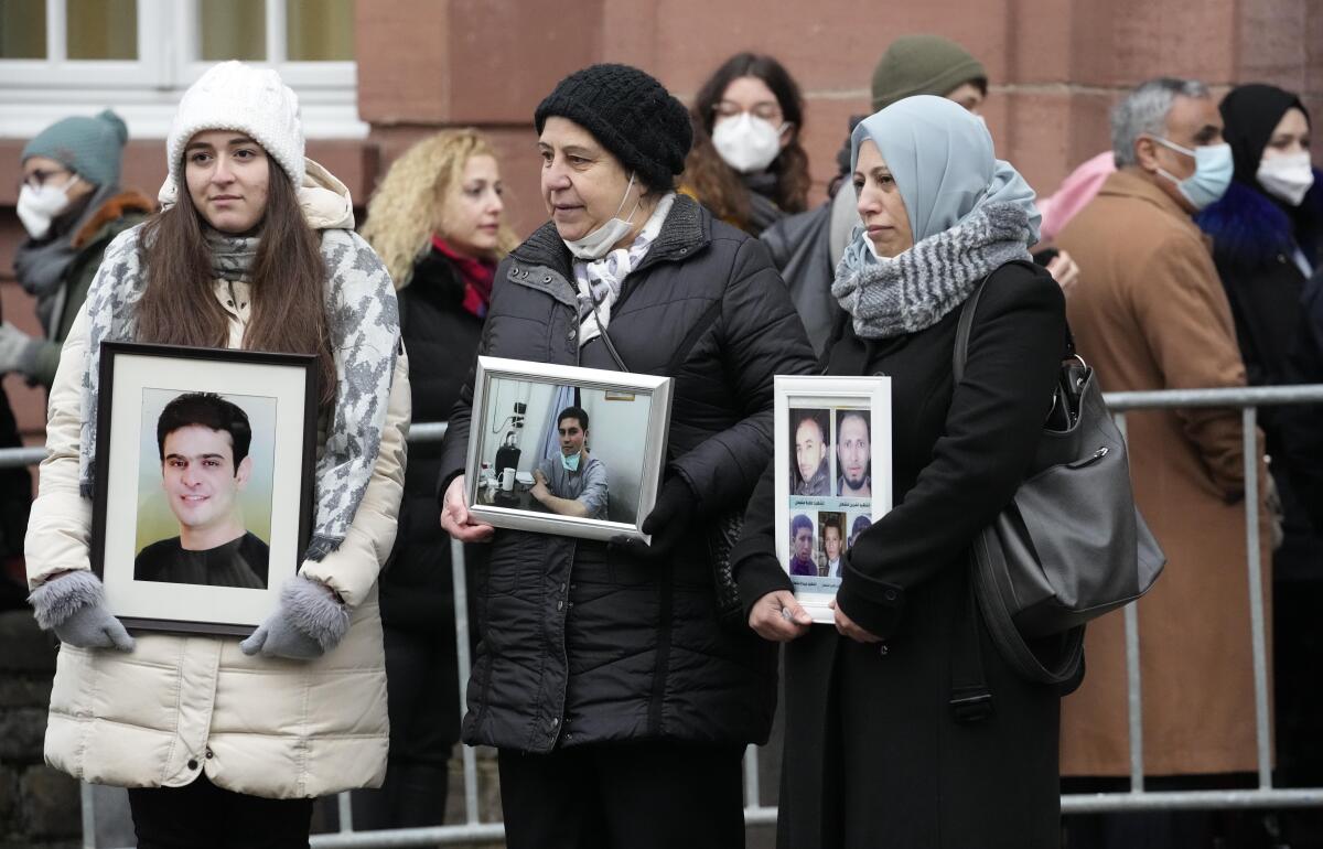 Three women hold pictures of relatives who died in Syria in front of a court building in Germany