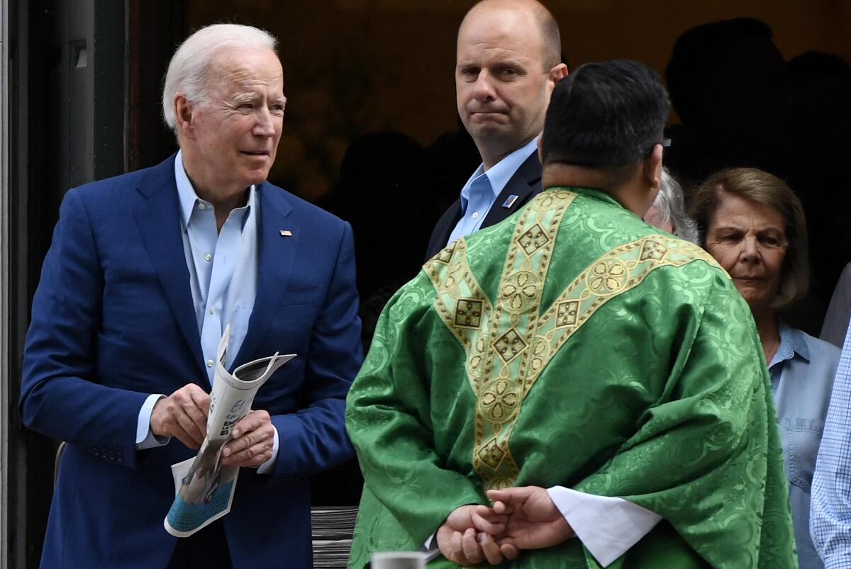 President Biden stands with other people near a clergyman.