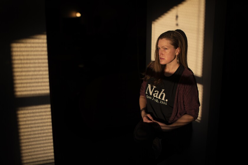 A woman poses for a portrait, framed by light from a window in a dark room