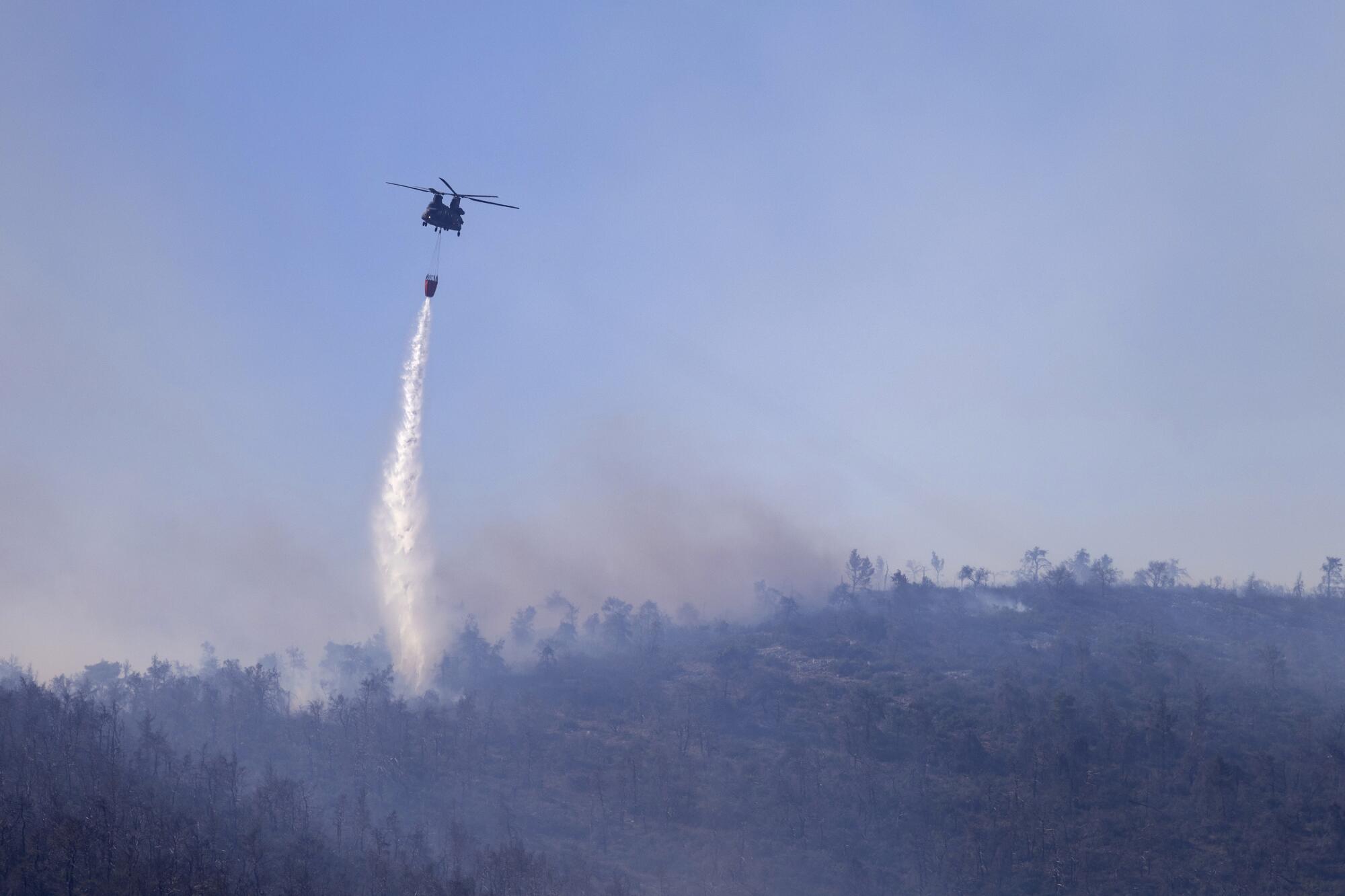 A helicopter dumps water over hazy, smoke-filled landscape