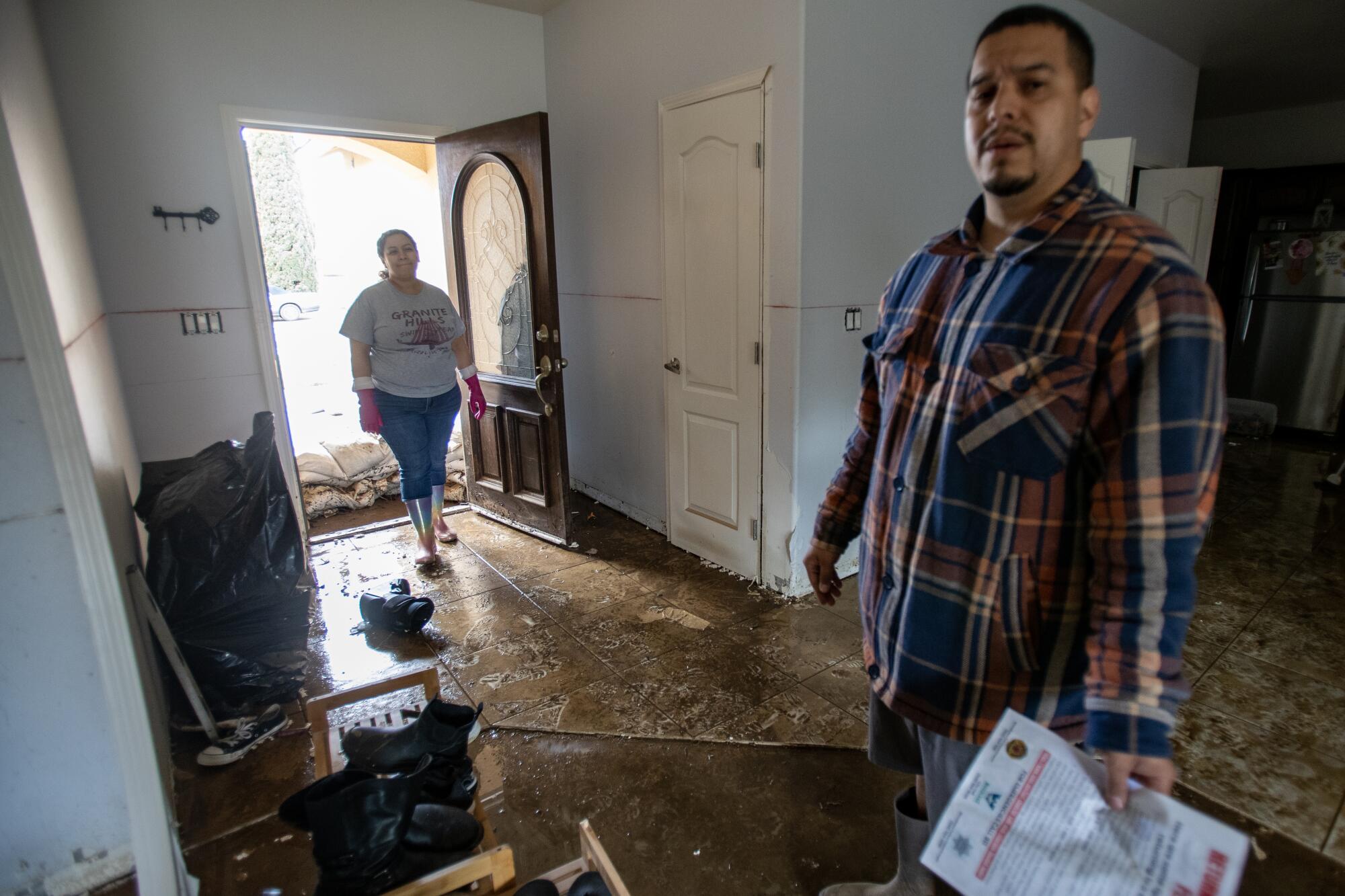 A couple stands in the entryway of a home that has been damaged by flooding.