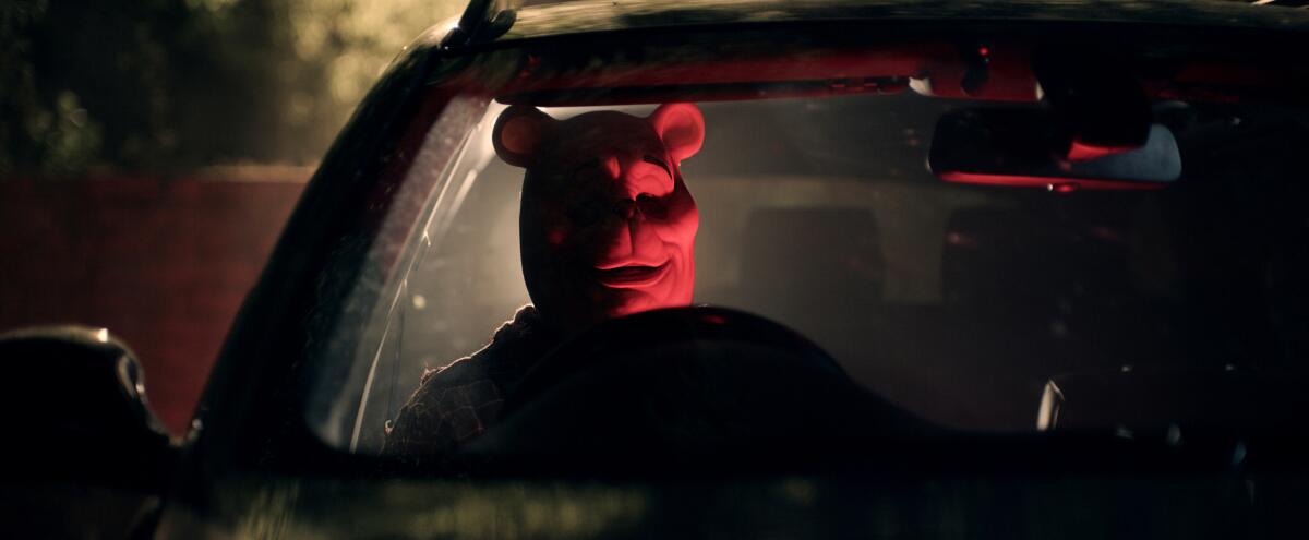 Person in a cartoon bear mask gazes through a car's windshield in red lighting