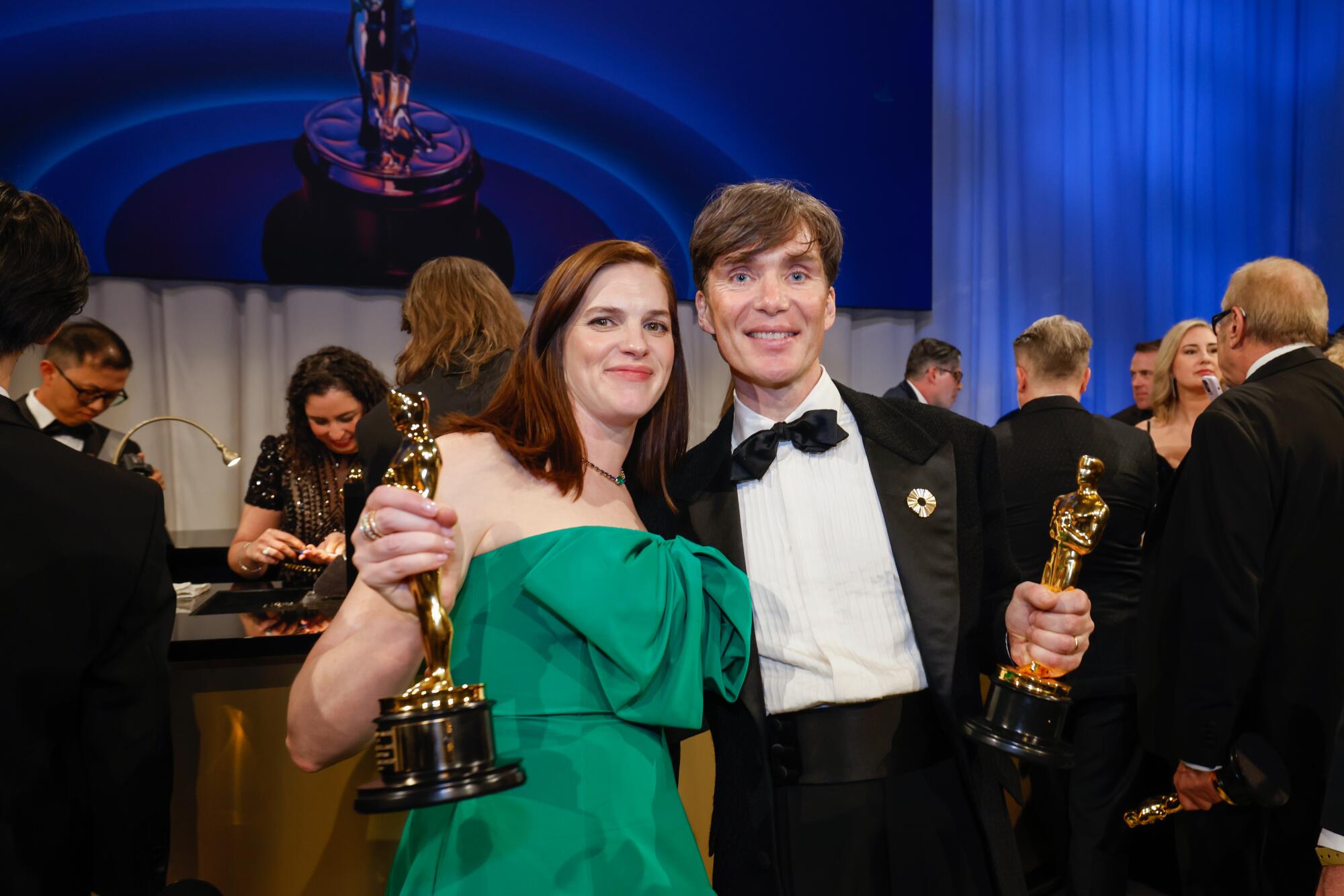 A woman and a man hold Oscars and smile for the camera.