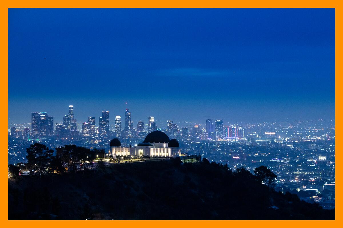 An aerial nighttime view of the lit-up Griffith Observatory with the lights of the city visible behind