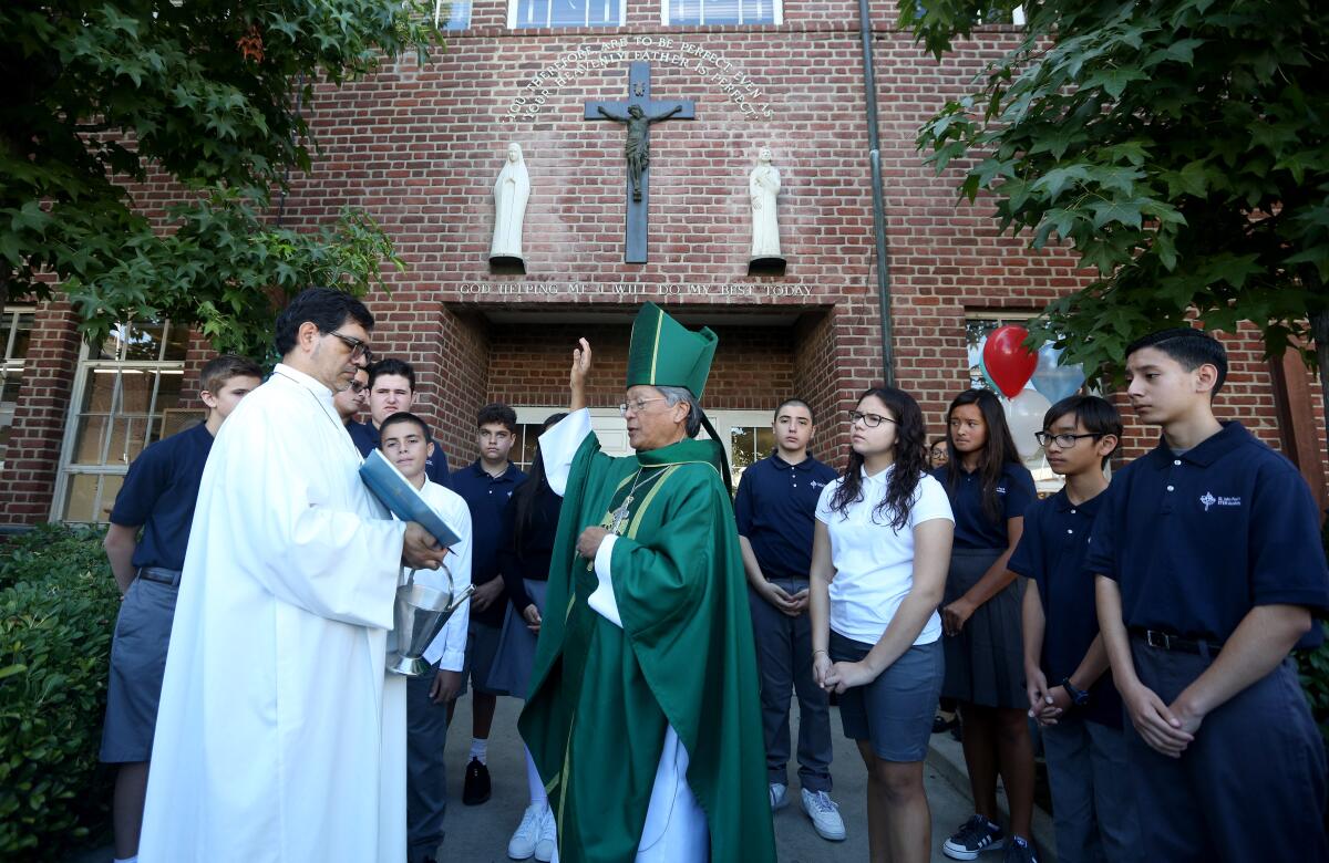 Surrounded by students, auxiliary Bishop Alex Aclan, with the Archdiocese of Los Angeles, center, says a prayer before blessing the newest area high school, St. John Paul II STEM Academy at Bellarmine-Jefferson, in Burbank on Tuesday.