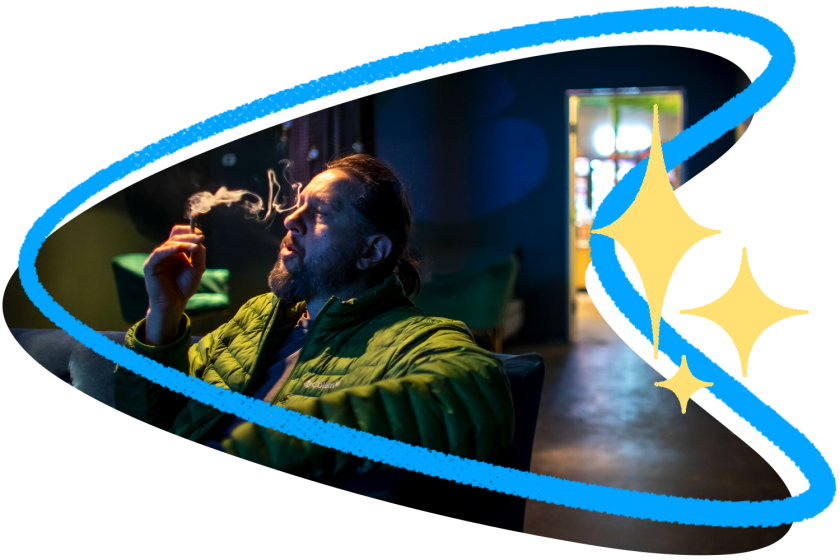 A man in a green puffer coat smokes a joint in a darkened room with a brightly lit doorway behind him, surrounded by retro blue frame illustration