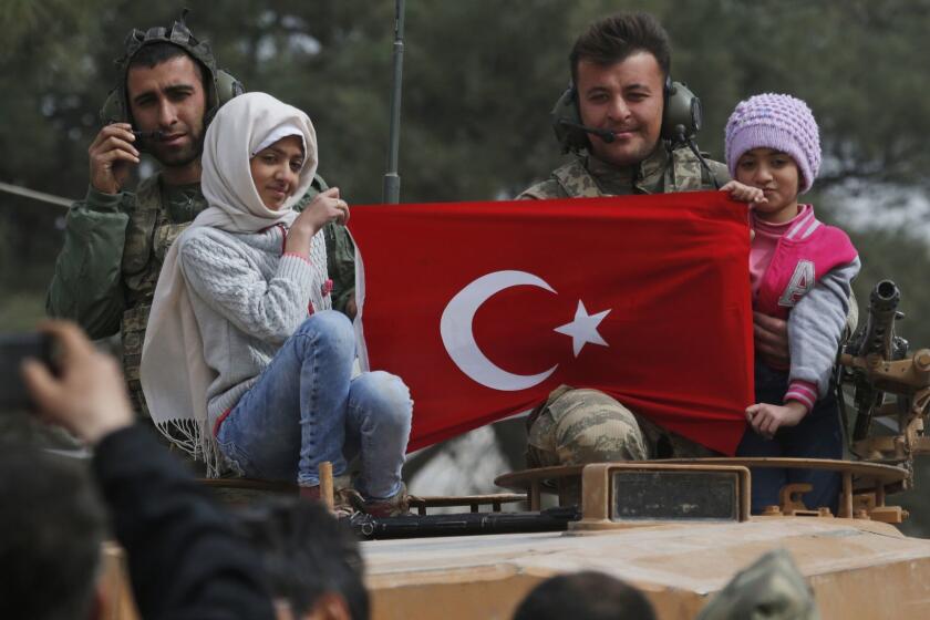 FILE - In this March 24, 2018 photo, Turkish soldiers atop a tank pose for pictures with Syrian children holding a Turkish flag, during a Turkish government-organized media tour, in the northwestern city of Afrin, Syria. Turkey is growing long-term roots in its northern Syrian enclave, nearly two years after its troops moved in, modeling the zone on its own towns and bringing in its own administrators and military, financial and security institutions. Turkey aims to keep out its nemesis, the U.S.-backed Syrian Kurdish militia known as the YPG. (AP Photo/Lefteris Pitarakis, File)