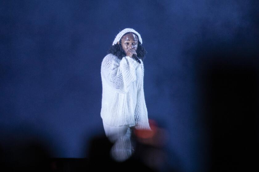 A man in a white beanie and sweater holding a microphone on a smokey stage