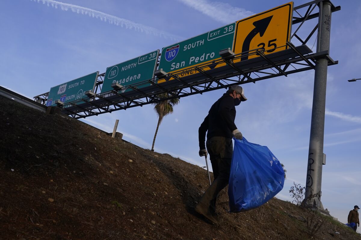 Califorina Gov. Gavin Newsom picks up litter on the side of the CA-101 freeway in Los Angeles Wednesday, Dec. 15, 2021. The cleanup comes amid growing frustration with homeless encampments that have sprouted under highway overpasses and near freeway exits and entry ramps throughout California in the past few years. (AP Photo/Damian Dovarganes)