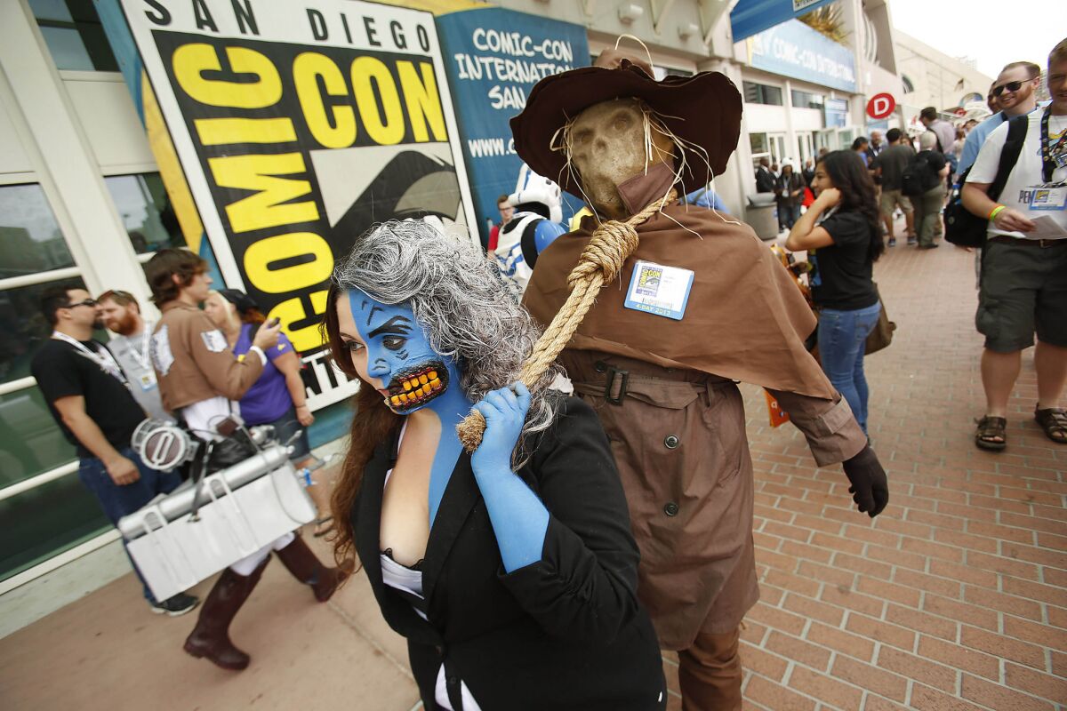 As Batman character Two-Face, Angie Rodriguez leads Jonathon Antone, cosplaying as Scarecrow, by the neck in front of the San Diego Convention Center at Comic-Con.