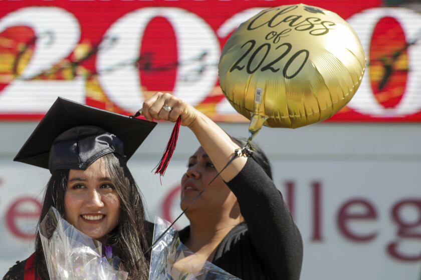 RANCHO CUCAMONGA, CA - MAY 20: Melissa Gomes, right, fixes the tassel as new graduate Sarah Anggraini gets ready for a photo at the marquee of Chaffey Colleges that held a drive through graduation on Wednesday, May 20, 2020 in Rancho Cucamonga, CA. Chaffey College handed out 600 “Grad Bags” at the Rancho Cucamonga campus, and around 170 each at the Chino and Fontana campuses. Chaffey will award about 6,400 degrees and certificates to the Class of 2020, the most awarded in the college’s history. (Irfan Khan / Los Angeles Times)
