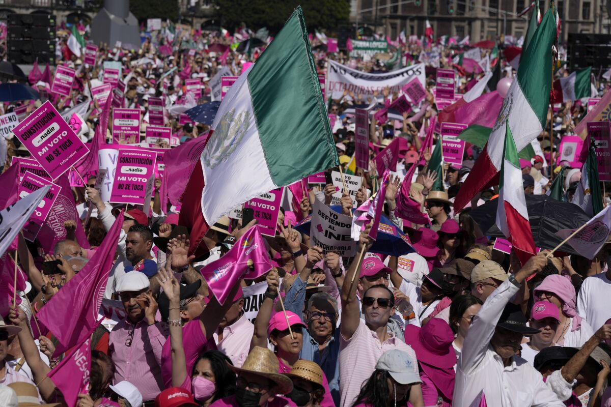 A crowd waves Mexico's green, white and red flag along with flags and signs in deep pink