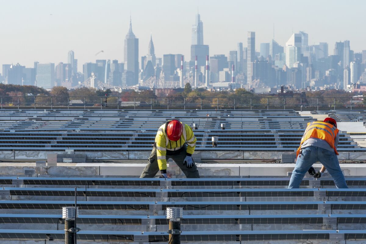 FILE - Framed by the Manhattan skyline electricians with IBEW Local 3 install solar panels on top of the Terminal B garage at LaGuardia Airport, Tuesday, Nov. 9, 2021, in the Queens borough of New York. As climate change pushes states in the U.S. to dramatically cut their use of fossil fuels, many are coming to the conclusion that solar, wind and other renewable power sources won't be enough to keep the lights on. Nuclear power is emerging as an answer to fill the gap as states transition away from coal, oil and natural gas to reduce greenhouse gas emissions and stave off the worst effects of a warming planet. (AP Photo/Mary Altaffer, File)