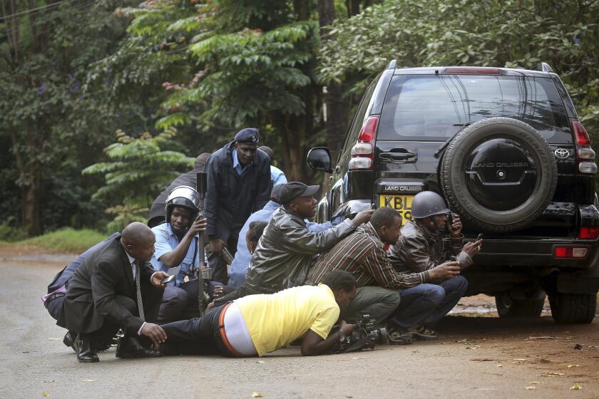 Kenyan security personnel and journalists duck behind a vehicle as heavy gunfire erupts from the Westgate shopping mall in Nairobi.