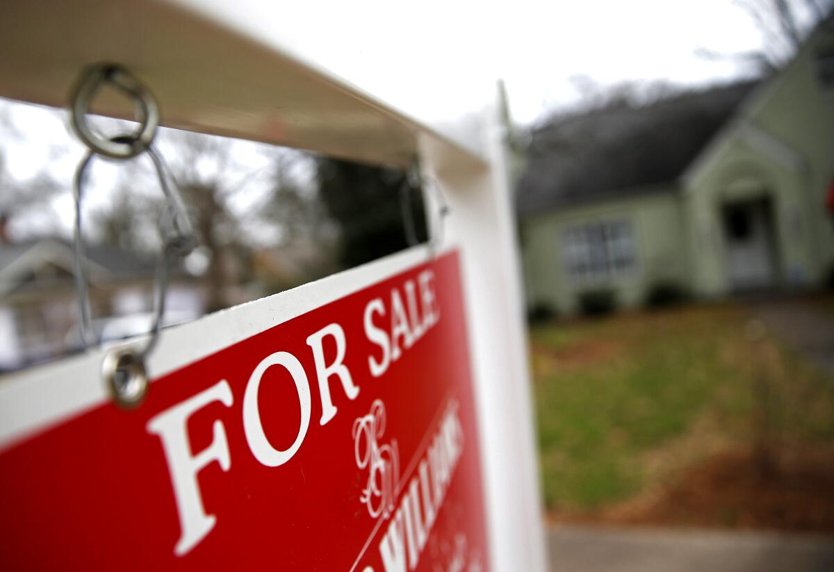 A "For Sale" sign hangs in front of a house