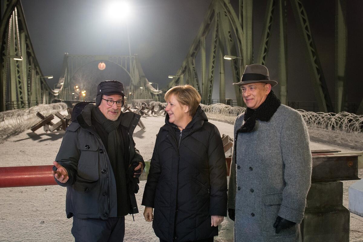 German Chancellor Angela Merkel talks on the set of the Glienicke bridge with director Steven Spielberg, left, and actor Tom Hanks.